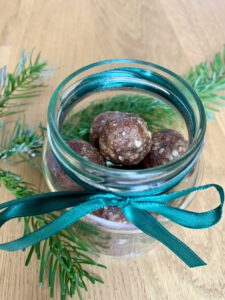 Festlich dekoriertes Schraubglas mit Lebkuchen Energy Balls, grüne Schleife und Tannenzweig im Hintergrund.