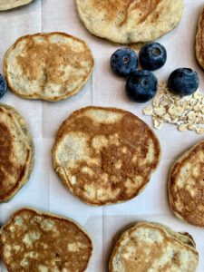 Kleine, goldbraun gebackene Pancakes auf weißem Untergrund dekoriert mit frischen Blaubeeren
