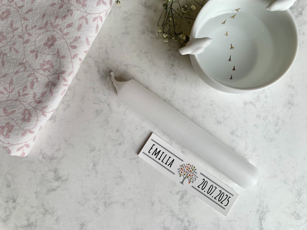 Gastgeschenke zur Taufe selbermachen Kerzentattoo anbringen Foto: Detailaufnahme des Aufbringens eines personalisierten Schriftzugs von einer Wasserschiebefolie auf eine weiße Mini-Stabkerze. Das Motiv wird als Kerzentattoo mit Wasser aufgebracht