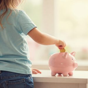 Kleinkind von hinten, das eine Münze in ein Sparschwein steckt. Besser als nur sparen für Kinder ist Geldanlegen in ETFs
