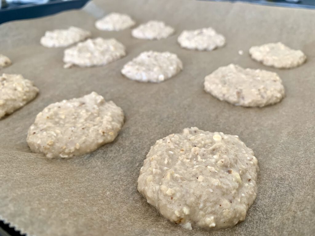 keksteig-ohne-zucker-apfelmus-kekse.jpg Roher Teig für Apfelmus Kekse ohne Zucker auf einem Backpapier portioniert - vegane und zuckerfreie Kekse für Babys und Kleinkinder schnell vorbereitet