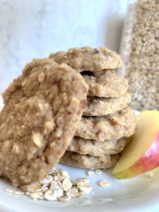 Gestapelte Apfelmus Kekse ohne Zucker, daneben eine Apfelscheibe und Haferflocken im Hintergrund - gesunder Snack für Kinder und Babys.