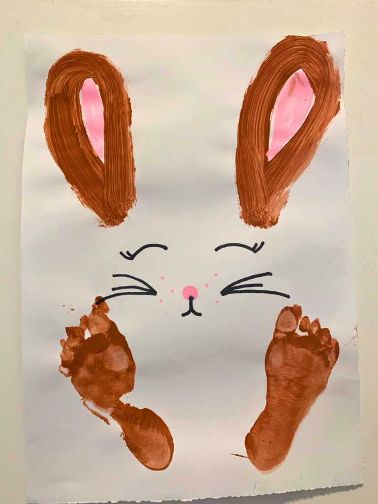 bastelideen-ostern-kinder-fußabdruck Nahaufnahme von selbstgemachten Fußabdruck-Hasen auf Papier, mit bunten Fingerfarben bemalt, als kreative Osterdekoration und Bastelidee für Ostern mit Kindern
