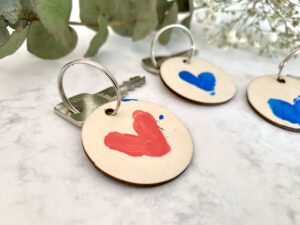 Drei DIY Schlüsselanhänger mit Fingerabdruck-Herz als Vatertagsgeschenk – zwei in Blau, einer in Rot, mit Schlüssel. Schnelle Bastelidee zum Vatertage