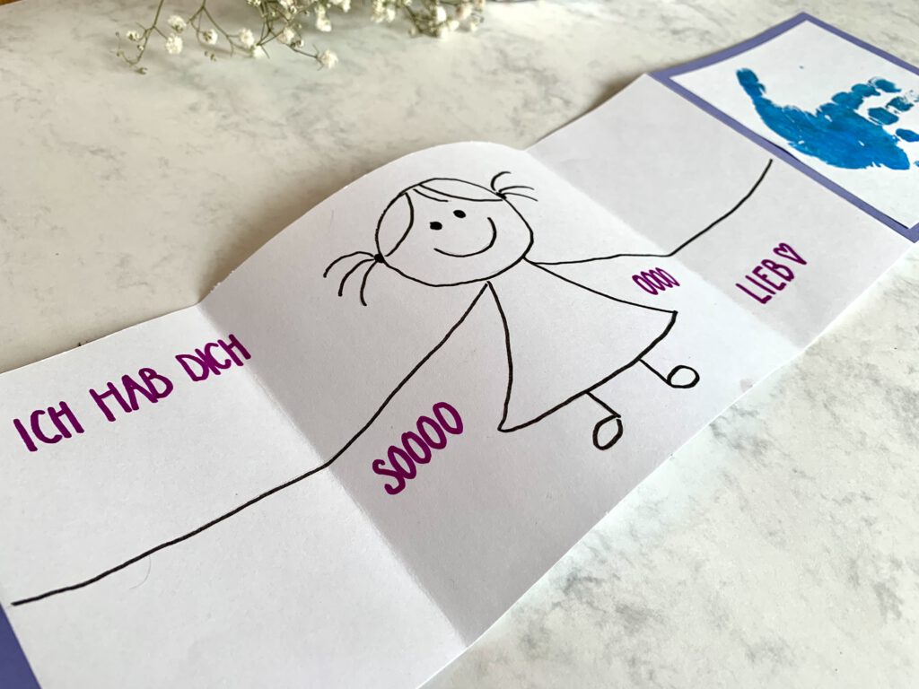 Ideen_zum_Vatertag Nahaufnahme der Innenseite der Vatertagskarte: Eine stilisierte Zeichnung eines Mädchens, das die Arme ausbreitet in Schwarz. In rosa Schrift der Text "ich hab dich so lieb". Vatertagskarte basteln mit Kleinkind.