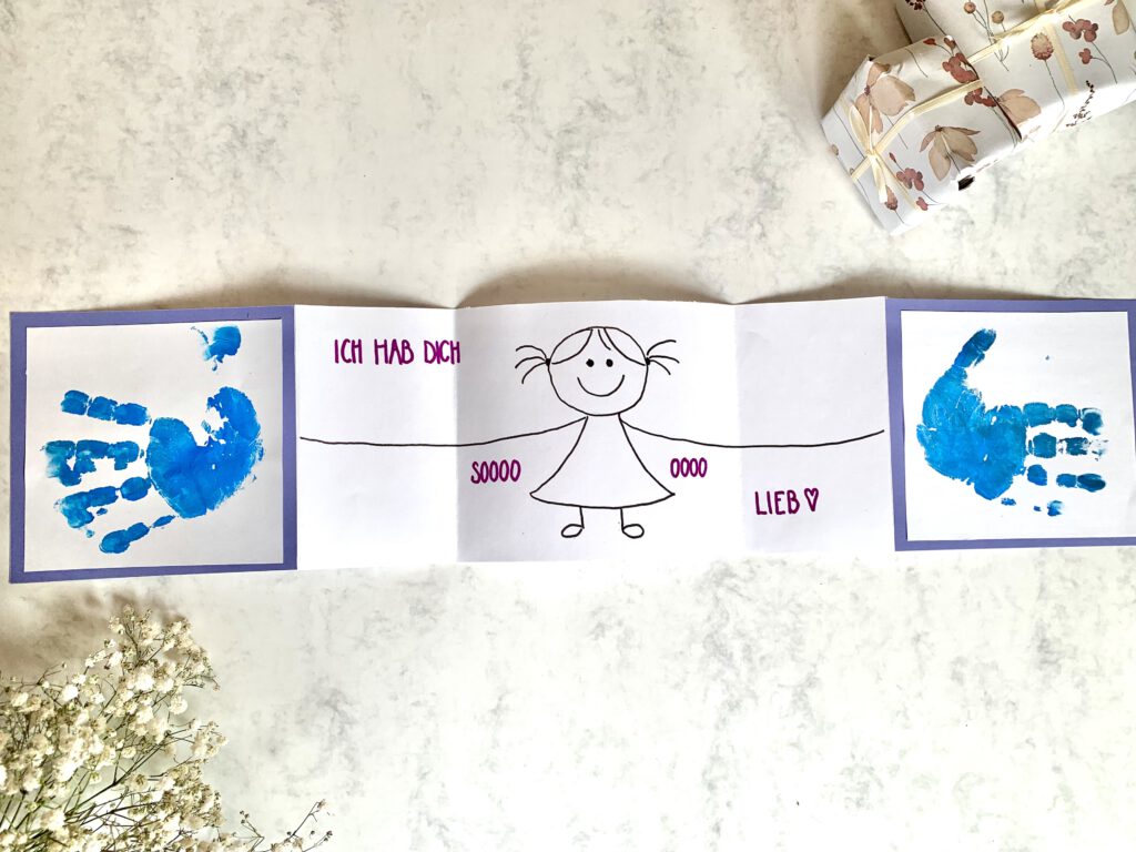 Vatertagskarte_basteln_Karte_aufgeklappt Fertige Karte zum Vatertag: Blaue Handabdrücke von Baby auf der Außenseite. Im Inneren der Klappkarte eine stilisierte Zeichnung eines kleinen Mädchens, das die Arme ausbreitet. Darüber der Schriftzug: "Ich hab dich so lieb". Eine einfache DYI Idee zum Vatertag, auch als Geschenk zum Vatertag.