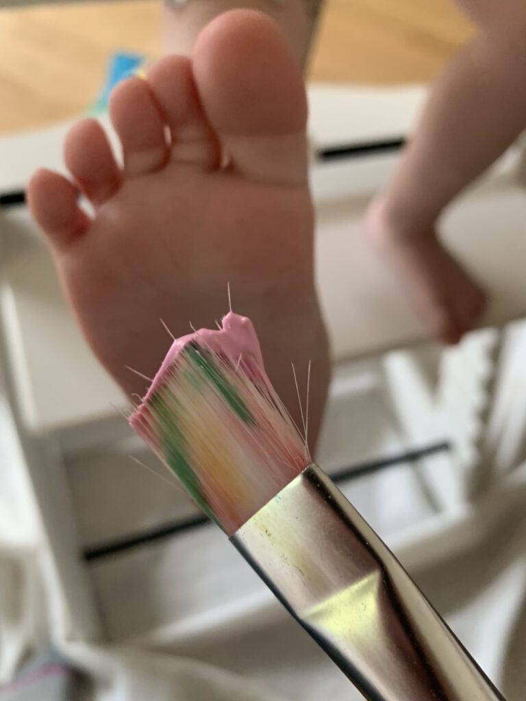 fuesse-mit-fingerfarbe-bemalen-kleinkind Kleinkind-Fuß wird mit bunter Fingerfarbe bemalt – Vorbereitung für Bastelprojekt. Karte basteln mit Kleinkind