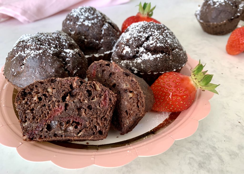 muffin-aufgeschnitten-ohne-zucker Schokomuffins ohne Zucker mit Banane gesüßt als gesunder Snack. Hier ein aufgeschnittener Muffin mit saftiger Textur und gefriergetrockneten Erdbeeren im Vordergrund, weitere zuckerfreie Muffins im Hintergrund