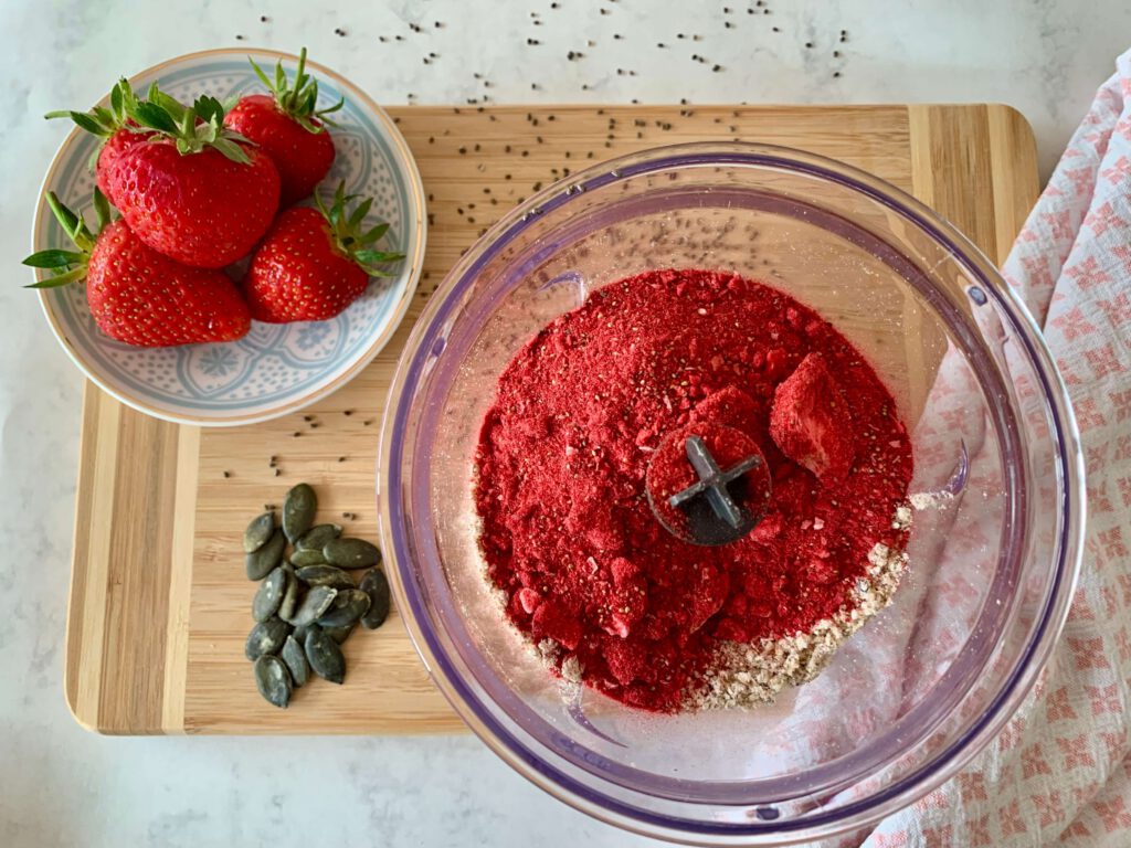 gefriergetrocknete-erdbeeren-instant-porridge-mix.jpg Gefriergetrocknete Erdbeeren werden in einen Mixer mit Nussmischung gegeben – veganes Porridge selber machen als schnelles Frühstück oder Meal Prep.