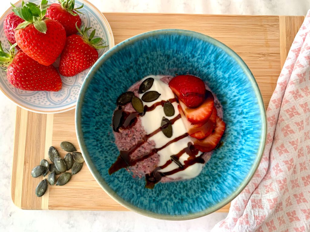 porridge-mit-joghurt-erdbeeren-kuerbiskernen-gesundes-fruehstueck.jpg Angerührtes Instant-Porridge in blauer Schüssel, getoppt mit Joghurt, Erdbeeren, Dattelsüße und Kürbiskernen – perfektes gesundes Frühstück oder Snack.