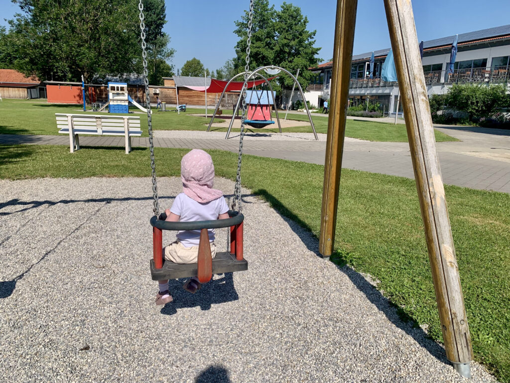 sommerausflug-mit-kleinkind-lechtalbad.jpg Kleinkind schaukelt im Freibad Lechtalbad. Ein Ausflugstipp für Familien in der Region Augsburg mit vielen Spielmöglichkeiten, Wasserspielplatz und seperatem Baby- und Kleinkindbecken. Badespaß für Familien.