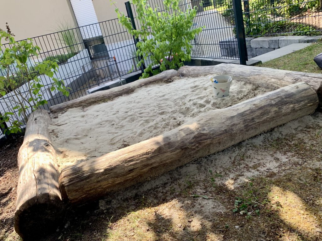 holzsandkasten-massiv-gross-spielbereich-kinder.jpg Großer Holzsandkasten mit massiven Seitenwänden – idealer Spielbereich für Kinder im Garten.