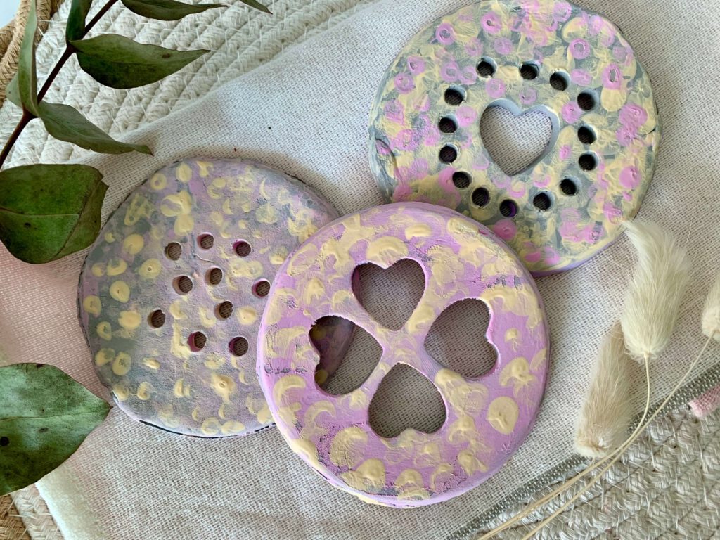 blumenretter-diy-kinder-basteln-bunte-scheiben.jpg Drei bunte Blumenretter von oben, bemalt in Lila, Rosa und Gelb – kreative Bastelidee mit Kleinkindern