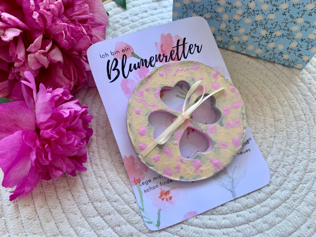 Geschenk basteln mit Kleinkindern: Blumenretter mit Schleife auf der Druckvorlage, im Hintergrund Geschenkverpackung und Blumen