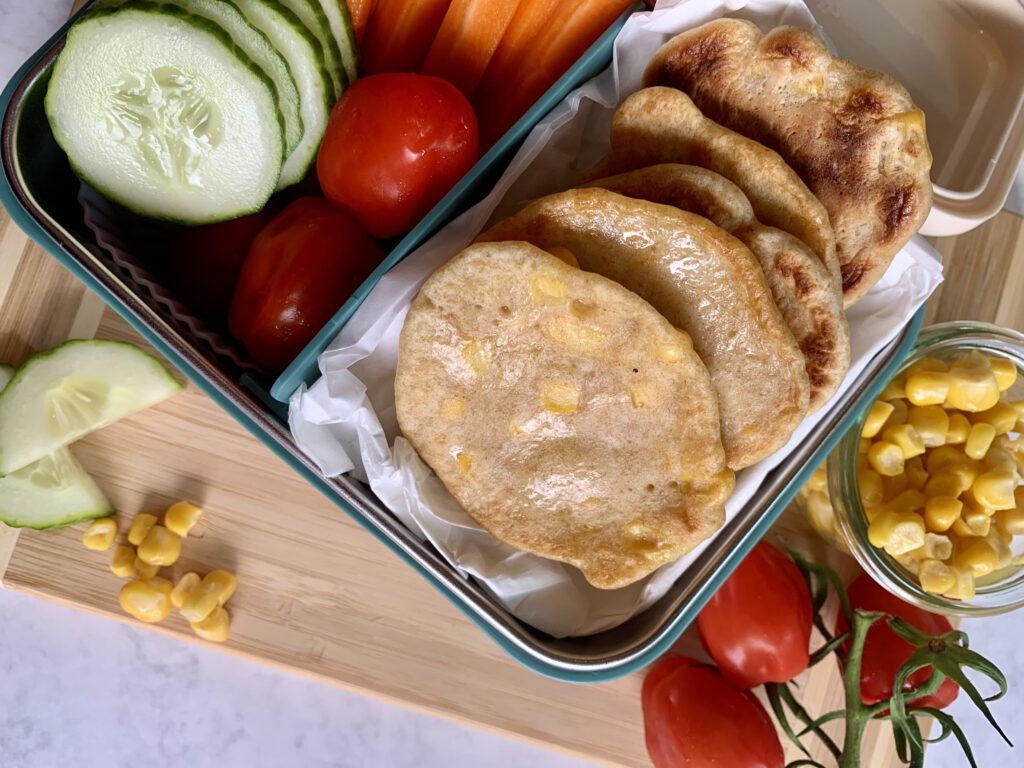 Familienfreundliche Lunchbox mit selbstgemachten Maispuffern und Gemüse