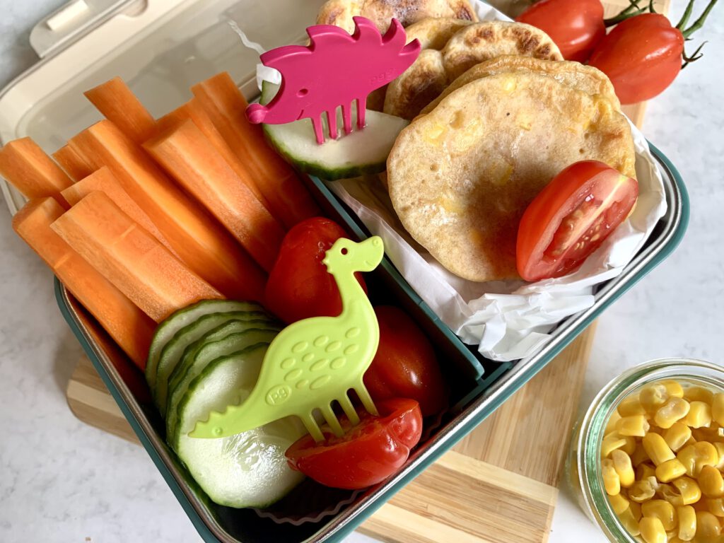 Ausgewogene Kita-Brotzeit: Maisküchle, Rohkost und bunte Snackpiekser – gesunde Lunchbox-Ideen für Kleinkinder.