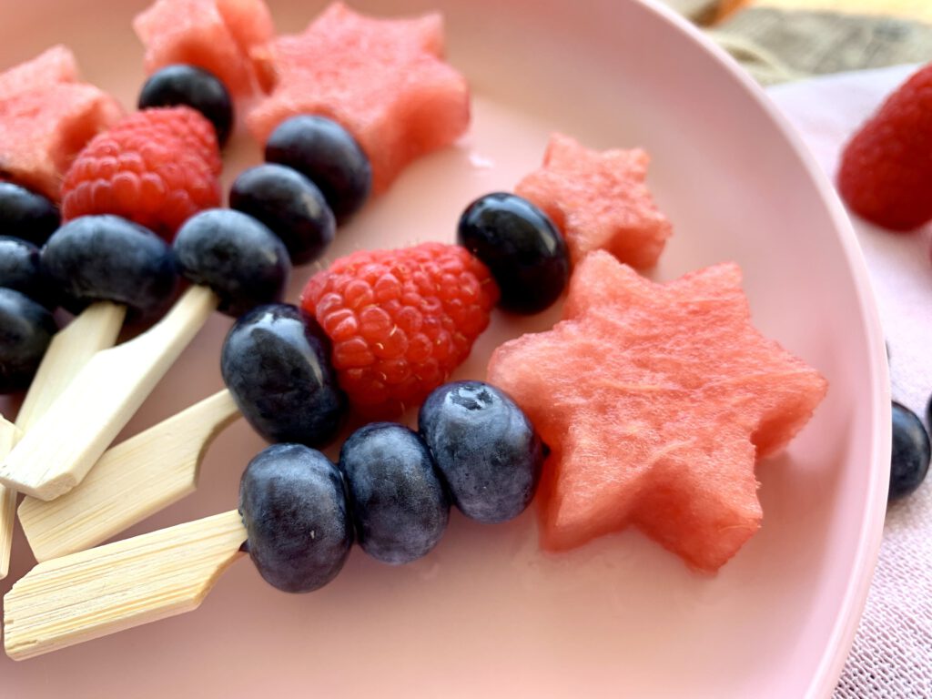 Zauberstäbe aus Obst. Auf kleine Spieße werden Blaubeeren, Himbeeren und Melone aufgesteckt. Wassermelone wurde in Sternform ausgestochen. Die Obstspieße bestehen aus Melone, Blaubeeren und Himbeeren. Die Melone wurde in Sternform ausgestochen. Eine schöne gesunde Snack Idee für Kinder, um Obst schmackhaft zu machen.