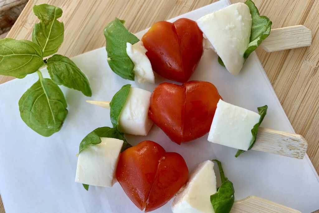 Gesunde Ideen für die Brotzeit für Kleinkinder: Herzen aus Cherry-Tomaten ergeben mit Mozzarella und Basilikum frische Caprese-Spieße.