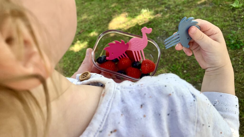 Ideen für die Kita-Brotdose: Kleinkind isst Himbeeren und Blaubeeren mit den Snack Pieksern von Pieksi und Griffel. Hier sind ein pinker Igel, ein rosa Dino und ein grauer Igel abgebildet.