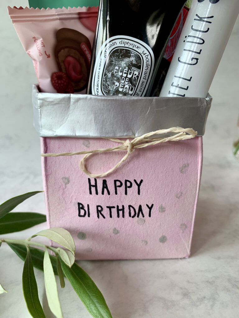 Detailaufnahme vom gebastelten Geschenkkörbchen aus Milchpackung mit rosa Farbe und Schleife. Schriftzug Happy Birthday. Ein kleines Geschenk zum Geburtstag für Mama, Freundin oder Kindergarten-Erzieherin.