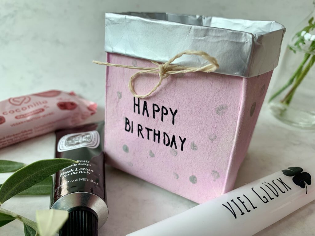 Selbstgemachtes Geschenkkörbchen aus Milchpackung mit daneben liegenden kleinen Geschenken. Kleines Geschenk zum Geburtstag oder Mitbringsel.