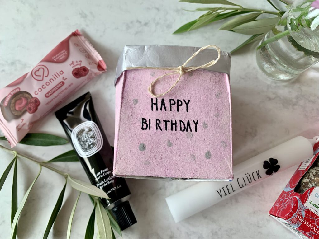 Blick von oben auf DIY Geschenkkörbchen aus Milchpackung gefüllt mit kleinen Geschenken. Bemalt in rosa mit dem Schriftzug Happy Birthday. Eine Geschenkidee für Freundin, Mama oder Erzieherin zum Geburtstag.
