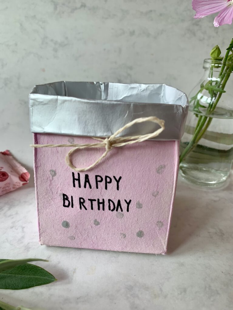 Selbst gebasteltes Geschenkkörbchen aus Milchpackung ohne Inhalt, in rosa mit der Beschriftung Happy Birthday