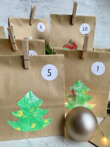 Fertige Kraftpapiertüten für selbst gemachten Adventskalender mit Kleinkind, dekoriert mit Tannenbäumen und Zahlen.