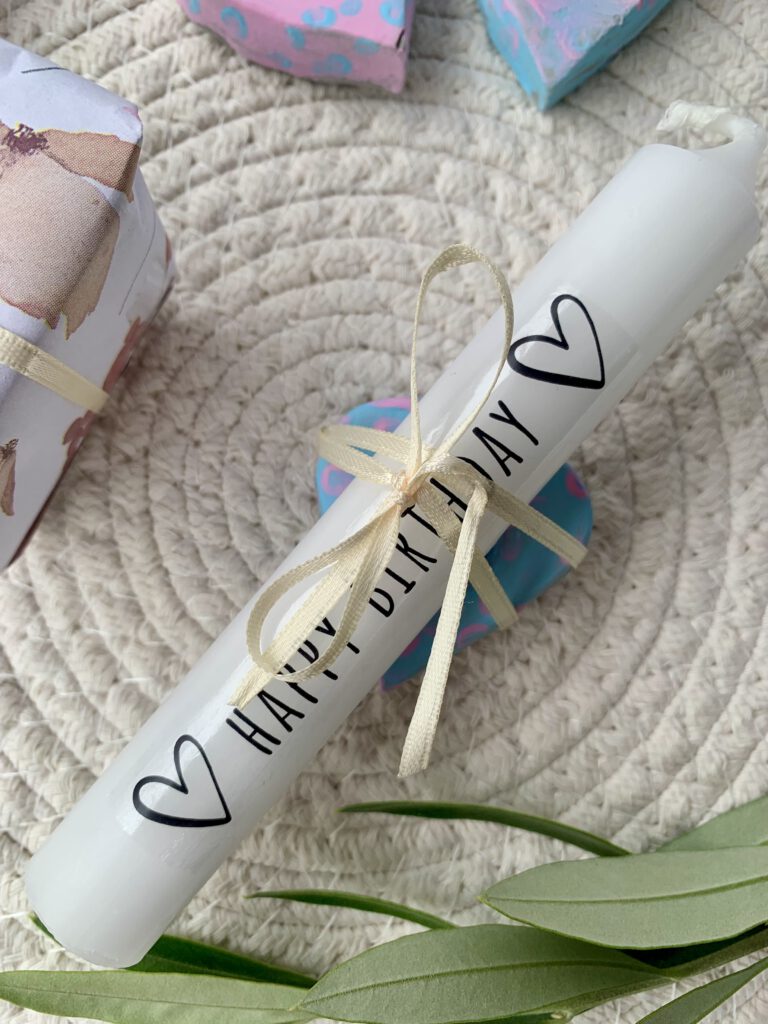 Selbst bedruckte weiße Kerze mit Schleife, dekoriert mit herzförmigen Kerzenhaltern aus Modelliermasse – DIY Geschenkidee für Geburtstag und Weihnachten.