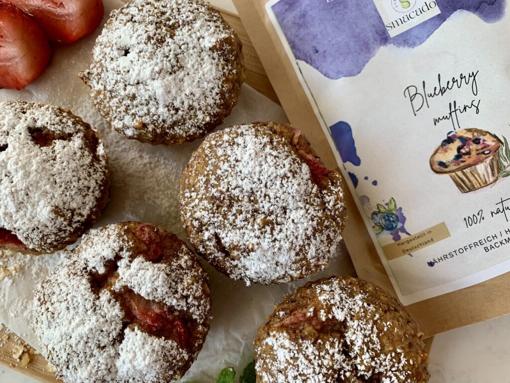 Fertige SMACADO Blueberry Muffins (als Erdbeer-Muffins abgewandelt) mit Backmischung im Hintergrund