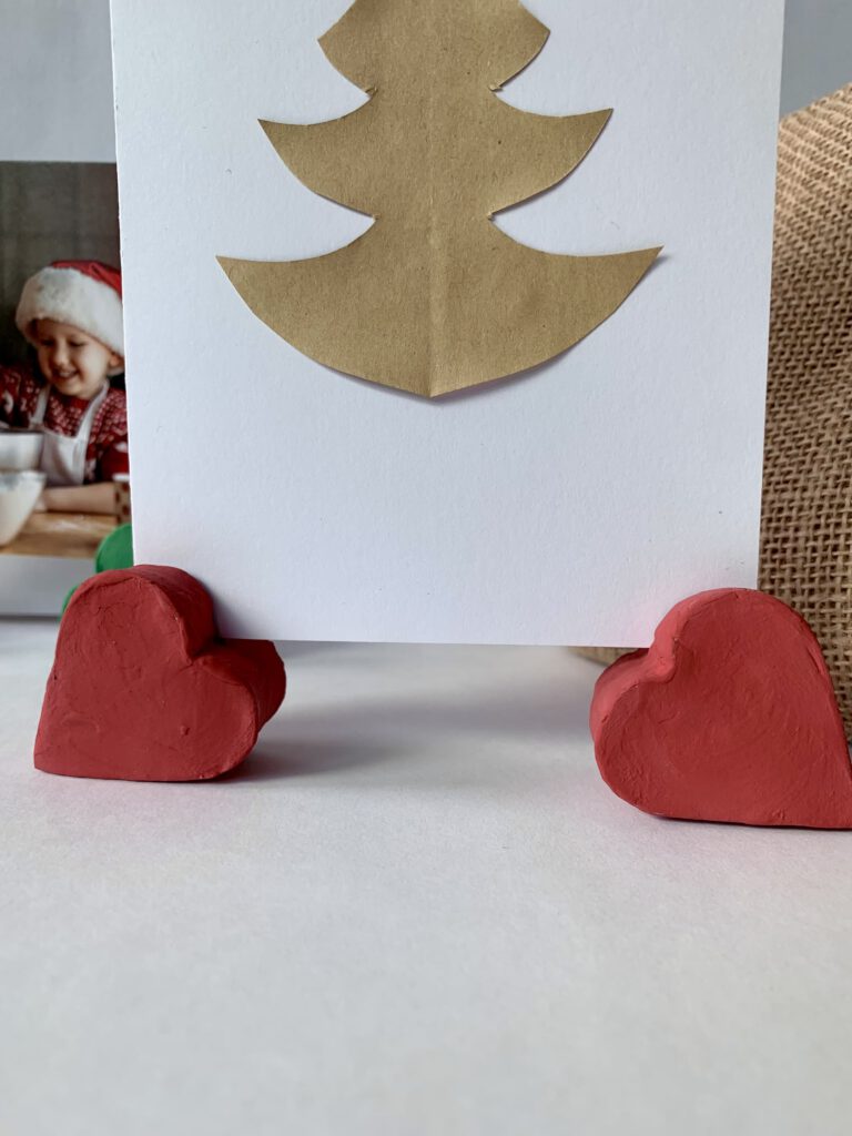 Zwei rote herzförmige Fotohalter mit Weihnachtskarte im Hintergrund