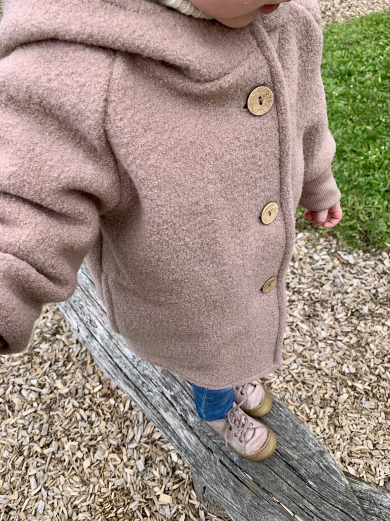 Kleinkind balanciert draußen mit der Wollwalkjacke – nachhaltige Kindermode mit Funktion und Stil.