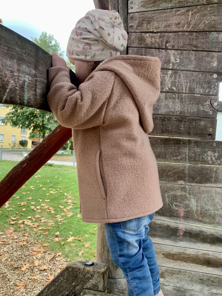 Kleinkind auf dem Klettergerüst von der Seite – Wollwalkjacke von Petit Cochon für aktive Kinder.