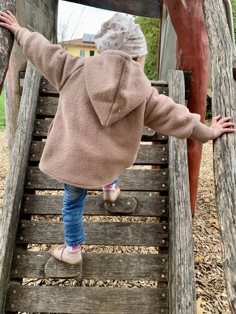 Kleinkind klettert und trägt Wollwalkjacke aus Wollwalk – langlebige und nachhaltige Kinderkleidung.