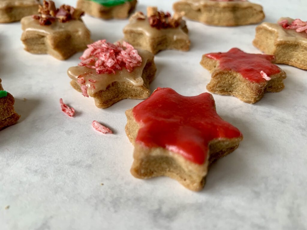 Sternplätzchen mit rotem zuckerfreiem Zuckerguss im Vordergrund, im Hintergrund Sterne mit roten Kokosflocken