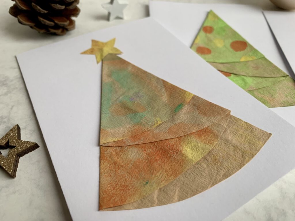 Fertige selbstgebastelte Weihnachtskarte mit Tannenbaum. Christbaum ist gefaltet aus einem bemalten Kaffeefilter. Bastelidee für Weihnachten mit Kindern.