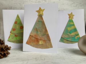 Drei stehende Weihnachtskarten mit gefalteten Tannenbäumen aus bemalten Kaffeefiltern und Stern-Dekoration.