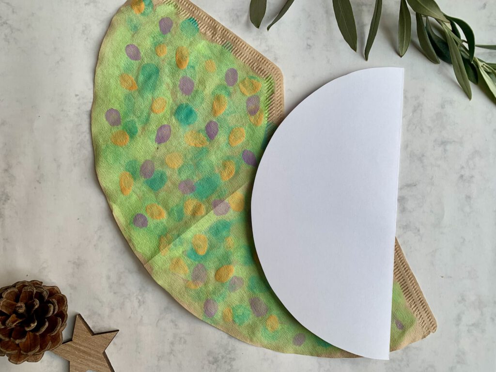 Bunt bemalter Kaffeefilter mit Pinsel und selbstgemachter Schablone für Tannenbaum-Weihnachtskarten.