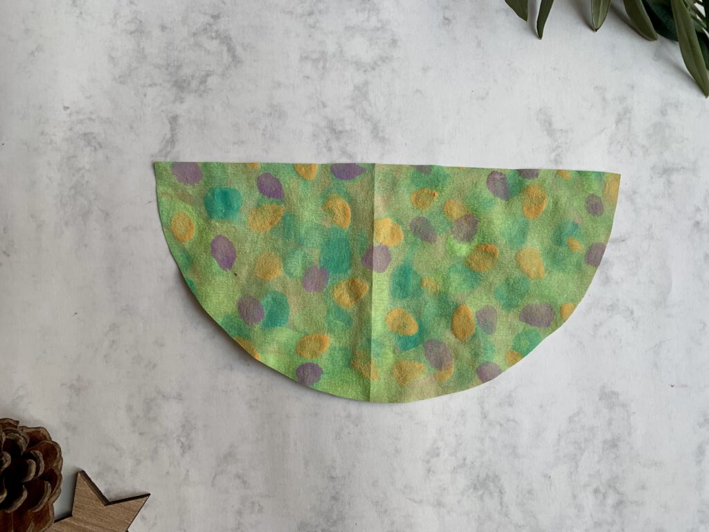 Aus bemaltem Kaffeefilter ausgeschnittener Halbkreis als Vorlage für den gefalteten Tannenbaum. Schritt für Schritt Anleitung Tannenbaum falten aus Papier für selbstgebastelte Weihnachtskarte