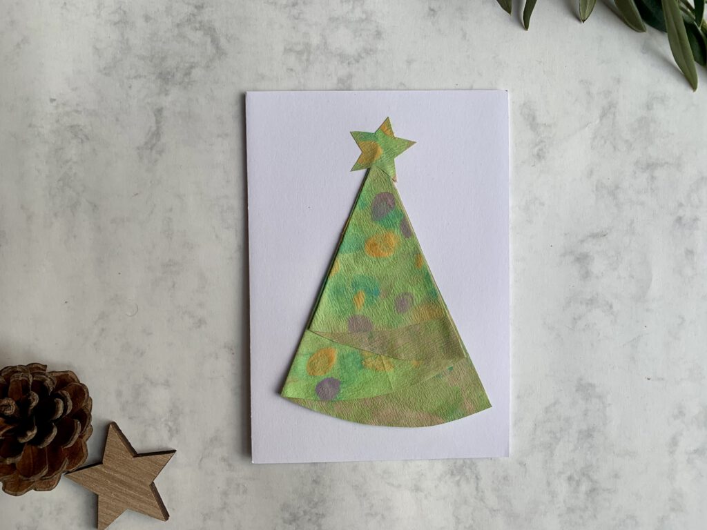 DIY Weihnachtskarte mit Kleinkind gebastelt. Aus bunt bemalen Kaffeefiltern wurde ein Tannenbaum gefaltet und auf eine Klappkarte geklebt. Perfekt für Weihnachtsbasteln mit Kindern und um persönliche Grüße zu versenden.