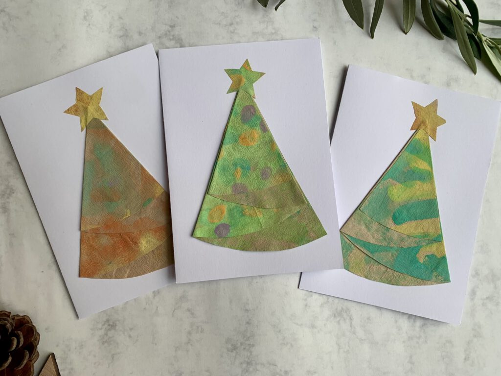 Drei fertige Weihnachtskarten mit Tannenbäumen aus bemalten Kaffeefiltern – nachhaltige Bastelidee für Kinder.