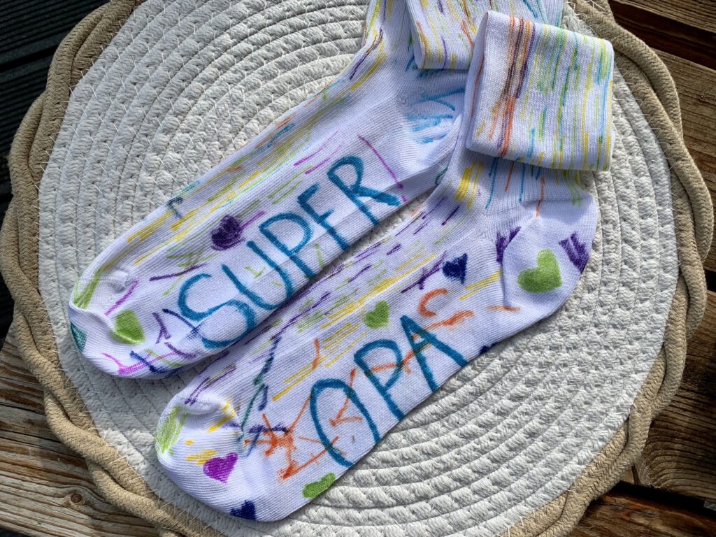 emalte weiße Socken mit bunten Punkten und Strichen sowie dem Schriftzug Super-Opa – selbstgemachtes Geschenk für Opa.