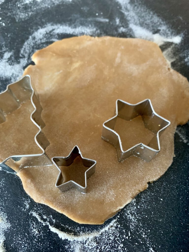 Backen mit Kindern: Ausgerollter Teig für zuckerfreie Weihnachtsplätzchen, mit Plätzchenausstechern (Sterne und Tannenbaum)