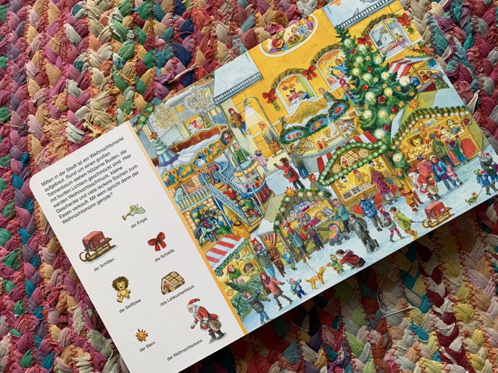 Aufgeschlagenes Weihnachts-Wimmelbuch mit Szene auf dem Weihnachtsmarkt – Sachen Suchen