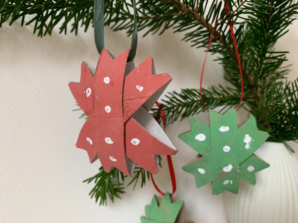 Verschiedene gebastelte Weihnachtssterne hängen an einem Tannenzweig, nachhaltige Weihnachtsdeko mit Kindern.