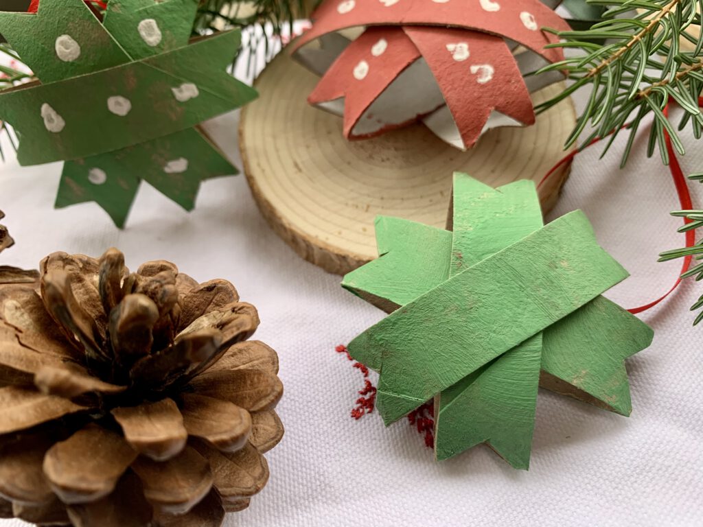 Einfache Sterne für Weihnachten gebastelt aus Toilettenpapierrollen. Zwei grüne Sterne im Vordergrung, ein roter Stern sowie Tannengrün im Hintergrund