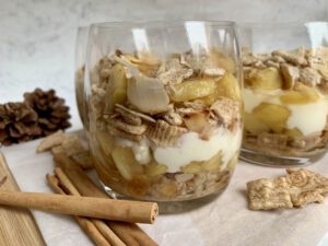 Weihnachtliches Dessert Rezept: Mehrere Dessertgläser mit Bratapfelcreme, Zimt und Tannenzapfen im Hintergrund