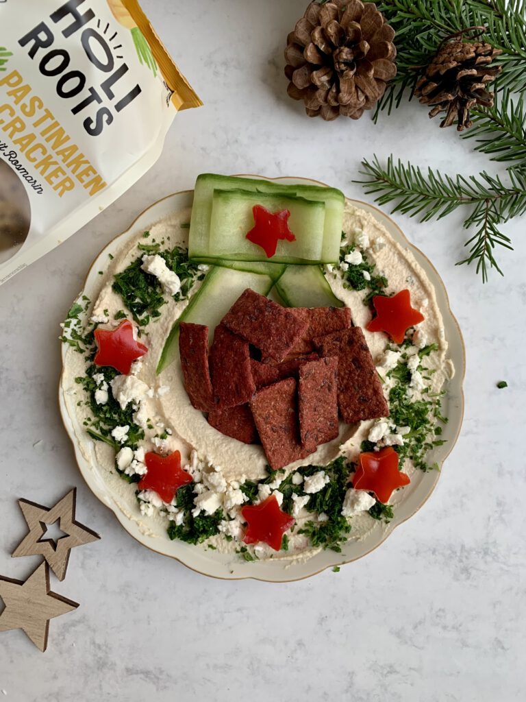 hummuskranz-weihnachten-holiroots-rote-bete-pastinake.jpg Weihnachtlicher Hummuskranz mit Holiroots Rote-Bete-Crackern und einer Packung Pastinaken-Cracker im Hintergrund. Vorspeise Weihnachten für viele Gäste.