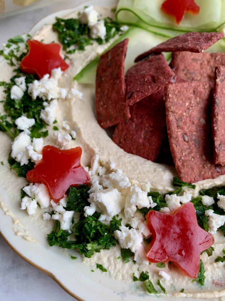 hummuskranz-detail-paprikasterne-feta-weihnachten.jpg Detailaufnahme vom Hummuskranz zu Weihnachten, dekoriert mit Petersilie, Feta und Paprikasternen. Perfekte Snackplatte für Weihnachten.