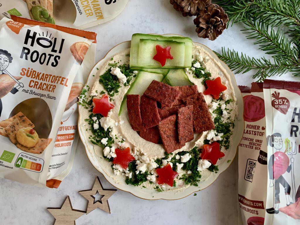 hummus-kranz-gurkenschleife-holiroots-weihnachten.jpg Hummus-Kranz mit Gurkenschleife, Paprikasternen und Holiroots Crackern als herzhafter Weihnachtssnack.